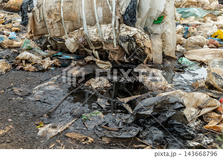 Piles of discarded plastic and trash cover the ground, with puddles of murky water accumulating among the debris, highlighting waste challenges Piles of discarded plastic and trash cover the ground, with puddles of murky water accumulating among the debris, highlighting waste challenges 143668796