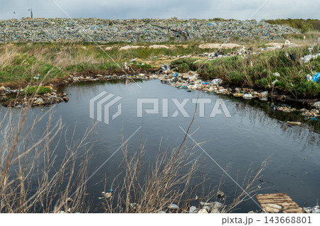 Dark, tainted water sits still in a neglected area, surrounded by heaps of discarded materials, showcasing environmental harm and urban waste 143668801