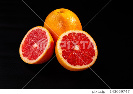 Fresh grapefruit whole and halved showing vibrant red pulp against black background with dramatic studio lighting 143669747