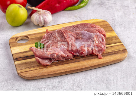 Raw turkey fillet on wooden cutting board with fresh vegetables including tomato, garlic, red and green peppers in soft natural light 143669801
