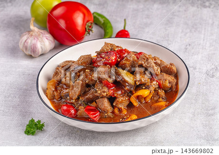 Hearty beef stew with eggplant, red peppers, and tomato sauce in white bowl, fresh garlic and parsley garnish on gray stone background Hearty beef stew with eggplant, red peppers, and tomato sauce in white bowl, fresh garlic and parsley garnish on gray stone background 143669802