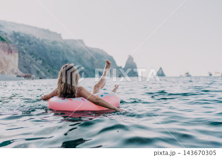 Woman, sea, vacation. Relaxing woman floats on inflatable ring in open sea, cliffs and boats background, copy space. Woman, sea, vacation. Relaxing woman floats on inflatable ring in open sea, cliffs and boats background, copy space. 143670305