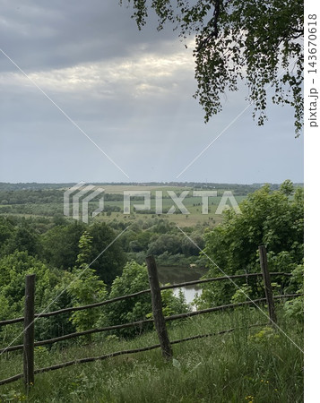 Countryside landscape with rustic wooden fence, rolling green fields, distant woodland, and cloudy sky Countryside landscape with rustic wooden fence, rolling green fields, distant woodland, and cloudy sky 143670618