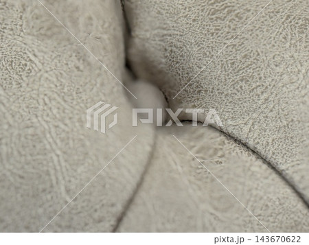 Closeup of soft cream fabric folds forming an abstract textured background with subtle shadows and curves Closeup of soft cream fabric folds forming an abstract textured background with subtle shadows and curves 143670622