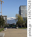 Urban plaza with modern apartment towers, construction crane, trees, and snowcapped mountains beneath blue sky Urban plaza with modern apartment towers, construction crane, trees, and snowcapped mountains beneath blue sky 143670628