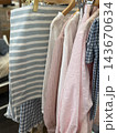 Pastel children's clothing hanging on wooden rack with striped, checked, pink, and white garments Pastel children's clothing hanging on wooden rack with striped, checked, pink, and white garments 143670634