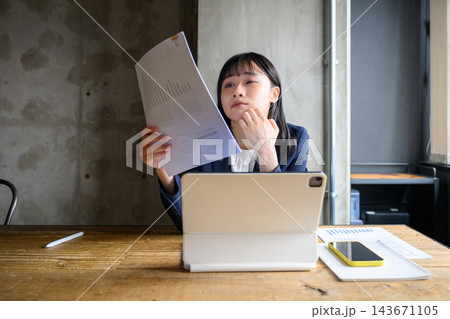書類のグラフを確認しながら考え込むオフィス勤務の女性会社員 143671105