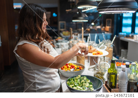 Woman chooses croissant, pancakes, salmon and cheese from a hotel breakfast buffet. Self service breakfast offers guests a variety of food during travel Woman chooses croissant, pancakes, salmon and cheese from a hotel breakfast buffet. Self service breakfast offers guests a variety of food during travel 143672101