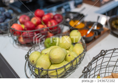 Fresh pears and red apples displayed in metal wire baskets at a hotel breakfast buffet. Healthy food choices and fruit selection for a balanced morning meal 143672102