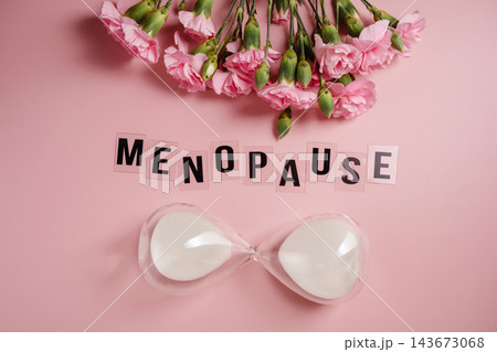 Menopause concept with hourglass and pink carnations on pastel background 143673068