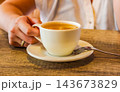 Hand Holding a White Cup of Tea at a Wooden Table for Cozy Cafe and Hospitality Concepts 143673829