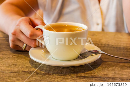 Hand Holding a White Cup of Tea at a Wooden Table for Cozy Cafe and Hospitality Concepts Hand Holding a White Cup of Tea at a Wooden Table for Cozy Cafe and Hospitality Concepts 143673829