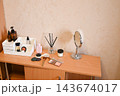 Makeup and skincare items arranged on a wooden table in a simple room during daytime 143674017