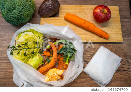 An overhead view shows folded biodegradable bags beside a bag of food scraps. Biodegradable material supports separate kitchen waste collection. An overhead view shows folded biodegradable bags beside a bag of food scraps. Biodegradable material supports separate kitchen waste collection. 143674709