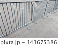 Metal crowd control barriers line a paved urban area 143675386