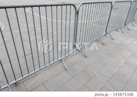 Metal crowd control barriers line a paved urban area 143675386