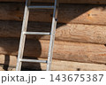 Aluminum ladder leaning against a sunlit log cabin wall 143675387