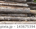 A pile of weathered gray logs stacked outdoors showing rough bark 143675394