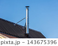 A shiny stainless steel chimney flue rises from a sloped metal roof 143675396