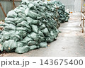 Large stacks of green sandbags line a pathway at a construction site 143675400