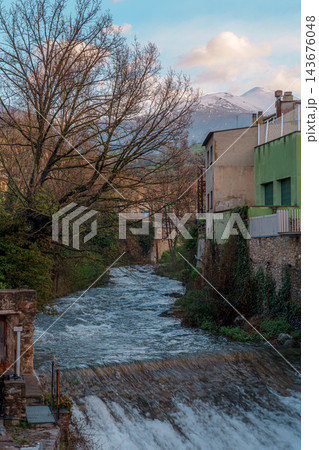 Freser river cascading over weir with bare tree and snowy Pyrenees peak in Ribes de Fresser 143676048