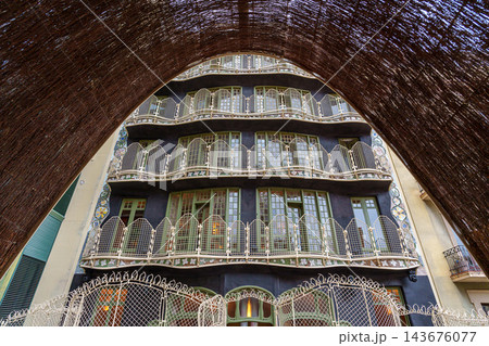 Rear facade of Casa Batllo with tiered curving balconies seen through an arch of woven brush Rear facade of Casa Batllo with tiered curving balconies seen through an arch of woven brush 143676077
