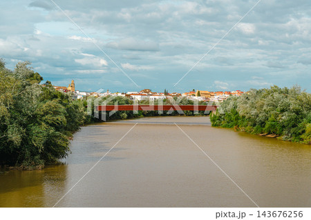 Rust colored steel footbridge crossing the Guadalquivir River with Cordoba old town skyline and bell tower beyond Rust colored steel footbridge crossing the Guadalquivir River with Cordoba old town skyline and bell tower beyond 143676256