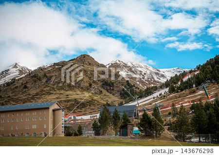 Chairlift line climbing a snow patched mountain slope with pine trees and blue sky in Vall de Nuria 143676298