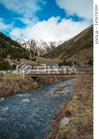 Wooden footbridge over a mountain stream with snowy peaks in Vall de Nuria Wooden footbridge over a mountain stream with snowy peaks in Vall de Nuria 143676300