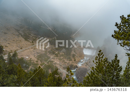 Mountain lake dam spilling water into a rocky gorge in fog seen from above in Vall de Nuria Mountain lake dam spilling water into a rocky gorge in fog seen from above in Vall de Nuria 143676318