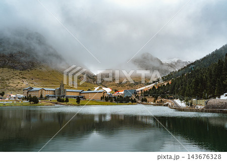 Sanctuary reflected in a calm mountain lake with fog covered peaks in Vall de Nuria 143676328