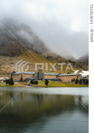 Large mountain sanctuary mirrored in a calm lake under fog covered mountain in Vall de Nuria 143676332