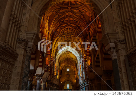 Gothic ribbed vault ceiling above red and white striped arches in a warmly lit aisle of the Mezquita of Cordoba 143676362