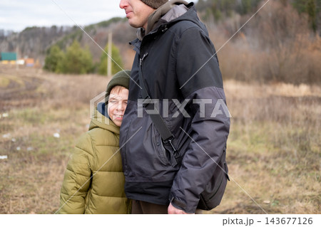 A smiling preteen boy hugs his father, feeling safe and protected during an autumn walk outdoors. 143677126
