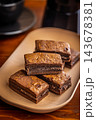 Stacked Homemade Chocolate Brownies on a Plate with Coffee Cup Close-Up in Cozy Cafe Setting 143678381