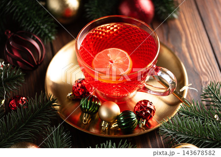 Hot fruit tea with lemon slice on golden saucer surrounded by christmas ornaments 143678582
