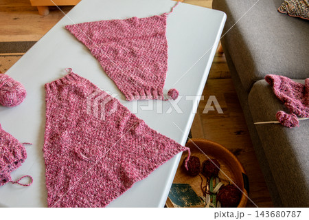 pink knitted triangle shawl pieces with yarn balls on table 143680787
