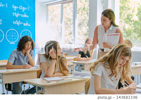 Math teacher helping teenage students at desk in classroom Math teacher helping teenage students at desk in classroom 143681336