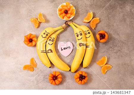 Adorable bananas in love, hugging each other, accompanied by a small heart labeled love and surrounded by butterflies and flowers made from mandarin oranges. This playful treat is perfect for children 143681347