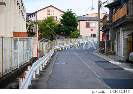 ガードレールと住宅が並ぶ静かな住宅街の道路、電柱と電線を正面から撮影した日常の街並みの写真素材 143682347