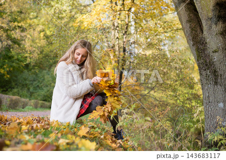 Young woman enjoys a colorful autumn walk in a city park, making a maple leaf wreath and playfully throwing fallen leaves. Seasonal lifestyle, outdoor recreation, wellness and the beauty of fall Young woman enjoys a colorful autumn walk in a city park, making a maple leaf wreath and playfully throwing fallen leaves. Seasonal lifestyle, outdoor recreation, wellness and the beauty of fall 143683117