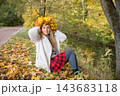 Young woman wearing a wreath of colorful maple leaves relaxes in an autumn park. Seasonal lifestyle portrait celebrating fall colors, outdoor wellness and the beauty of nature. 143683118