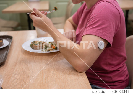 A woman with a continuous glucose monitor is eating in a cafe.  143683341