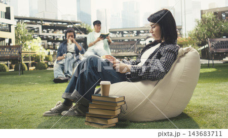 Student, reading and books as a woman relaxes on a beanbag with an open book and stacked textbooks nearby on a lawn. Independent learning, literacy and campus life suit peaceful study outdoors. Student, reading and books as a woman relaxes on a beanbag with an open book and stacked textbooks nearby on a lawn. Independent learning, literacy and campus life suit peaceful study outdoors. 143683711