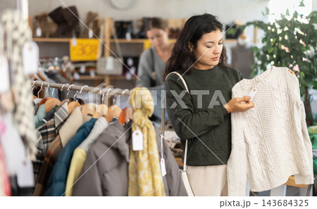 Latin girl is busy looking at clothes items in store, choose sweater 143684325