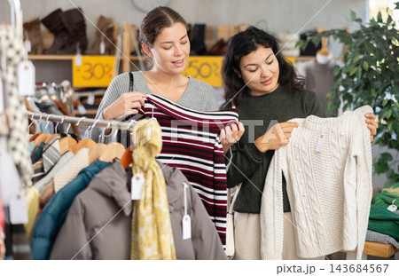 Latin woman with female companion is busy looking at clothes items, choose winter sweater Latin woman with female companion is busy looking at clothes items, choose winter sweater 143684567