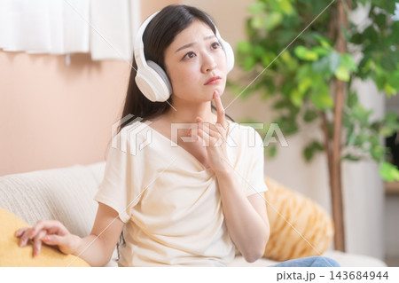 ヘッドホンを着け、指を顎に当てて考える女性 143684944