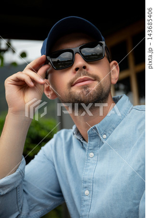 Man wearing sunglasses and a blue shirt relaxing outdoors 143685406