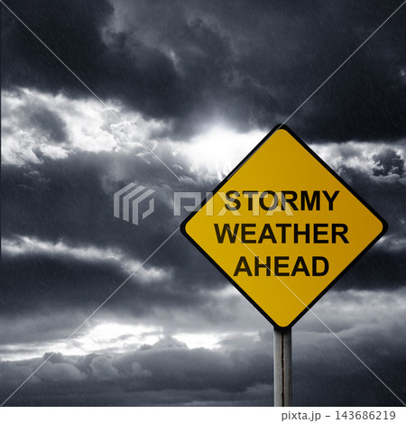 A yellow caution sign that reads STORMY WEATHER AHEAD stands against a dramatic, dark and rainy sky with ominous storm clouds. Storm background 143686219