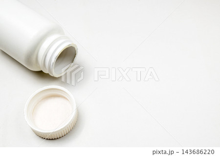 An open white plastic medicine bottle with its cap beside it, set against a clean white background, ideal for healthcare and pharmaceutical concepts. 143686220